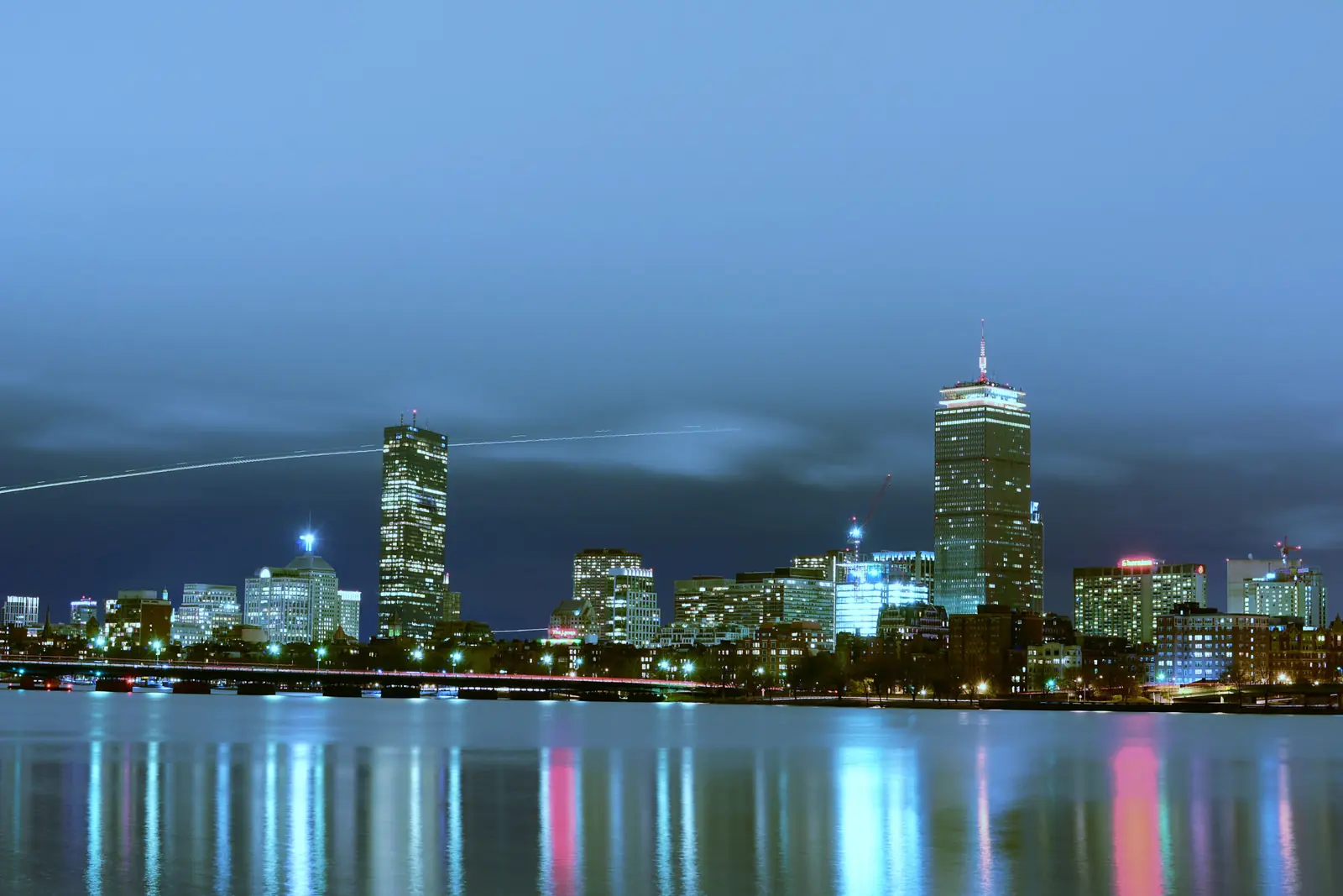 The Boston skyline lit up at night, reflected on the water