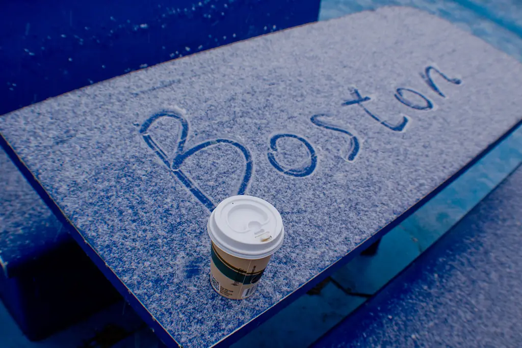 The word Boston written in fresh snow beside a coffee cup