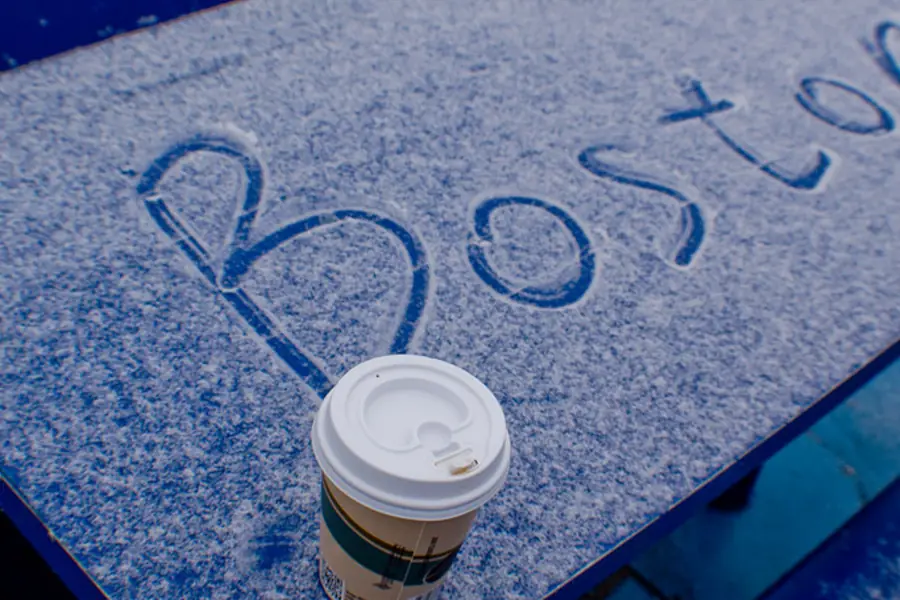 The word Boston written in fresh snow beside a coffee cup